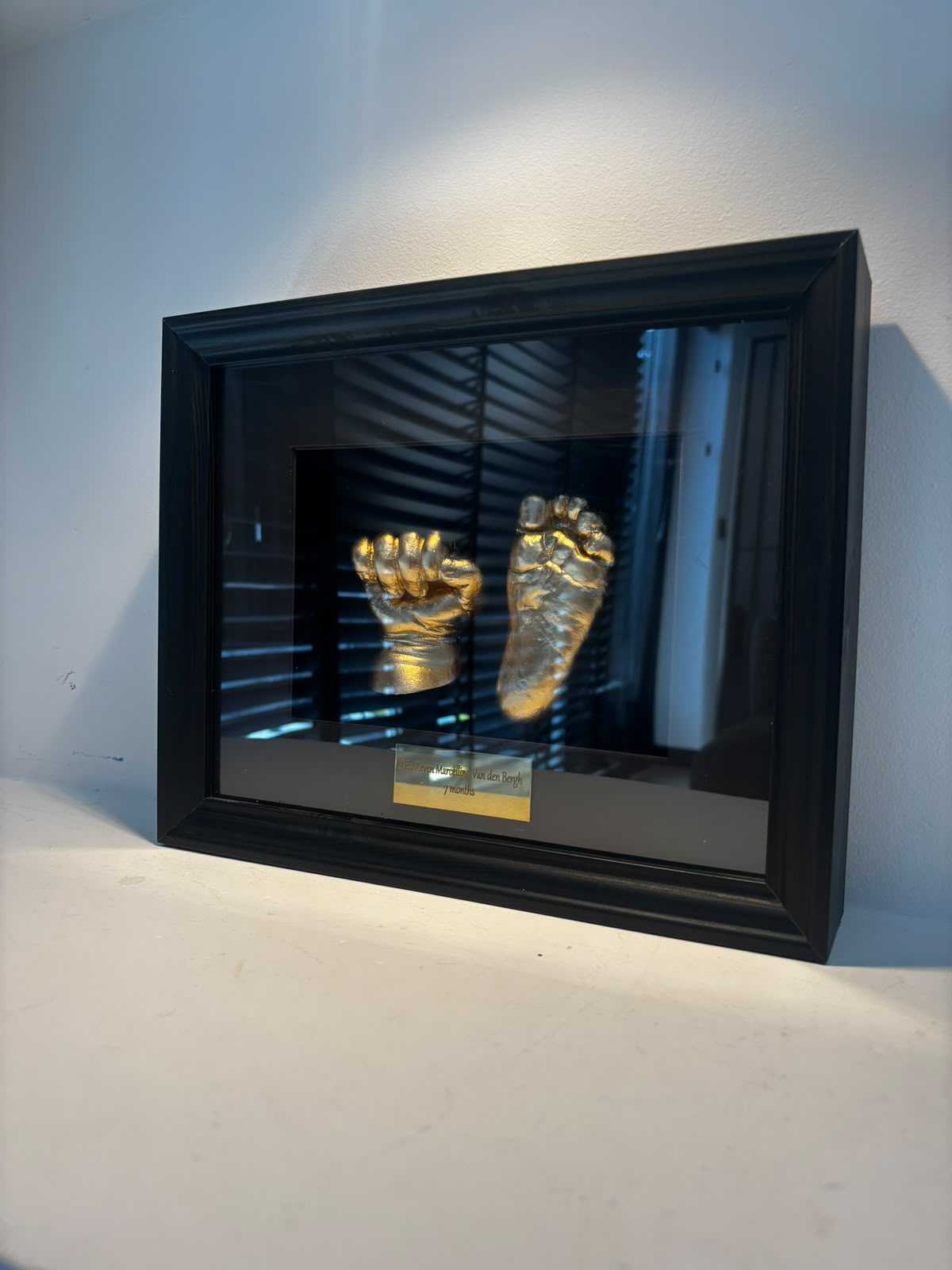 Zwarte 3D-lijst met gouden gipsafdrukken van een handje en voetje, schuin van dichtbij gefotografeerd